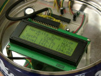 The NerdKits microcontroller breadboard and LCD are mounted inside a holiday cookie tin.